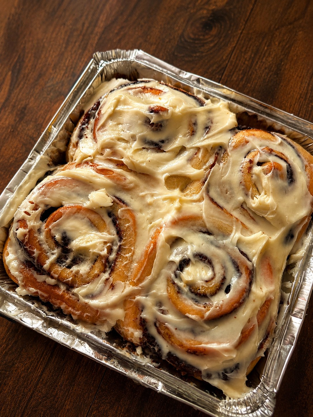 Four freshly frosted No Crumbs Bakery cinnamon rolls in a tray