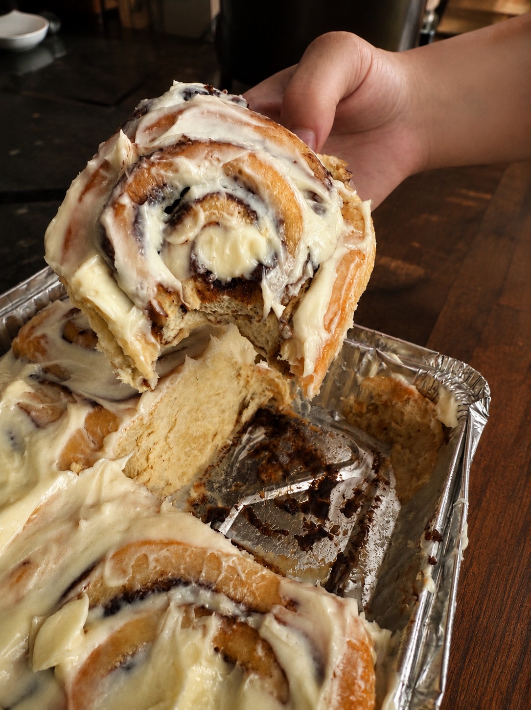A warm cinnamon roll being lifted from a freshly baked tray