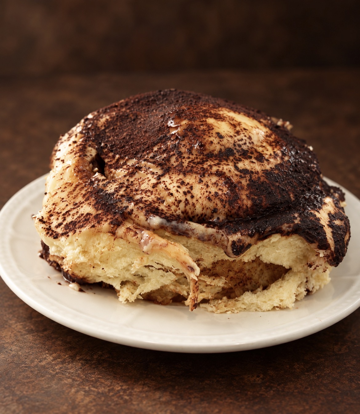 A No Crumbs tiramisu roll on a plate, topped with creamy frosting and cocoa